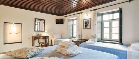 Habitación de hotel con dos camas, un escritorio, una silla, un televisor y ventanas grandes con cortinas.