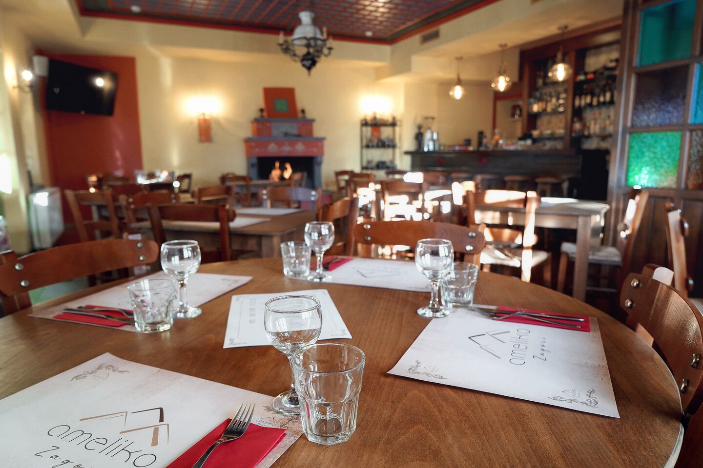 A restaurant interior with wooden tables, chairs, and a bar area in the background.