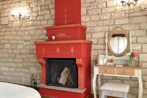 A room with a stone wall, a red fireplace with decorative elements, a wooden dresser with a mirror, and a bench. - Ameliko Zagori (Zagori)