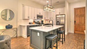 Una cocina moderna con armarios blancos, una isla central con taburetes, electrodomésticos de acero inoxidable y una lámpara colgante.