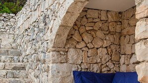 A stone-built outdoor seating area with a mattress and pillows, surrounded by stone steps and a pool. - Villa La Mecca Leuca Seaside villa with pool (Gagliano del Capo)