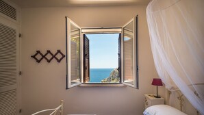 A bedroom with a bed, a window with an open view of the sea, a bedside table with a lamp, and a decorative wall piece. - Villa La Mecca Leuca Seaside villa with pool (Gagliano del Capo)