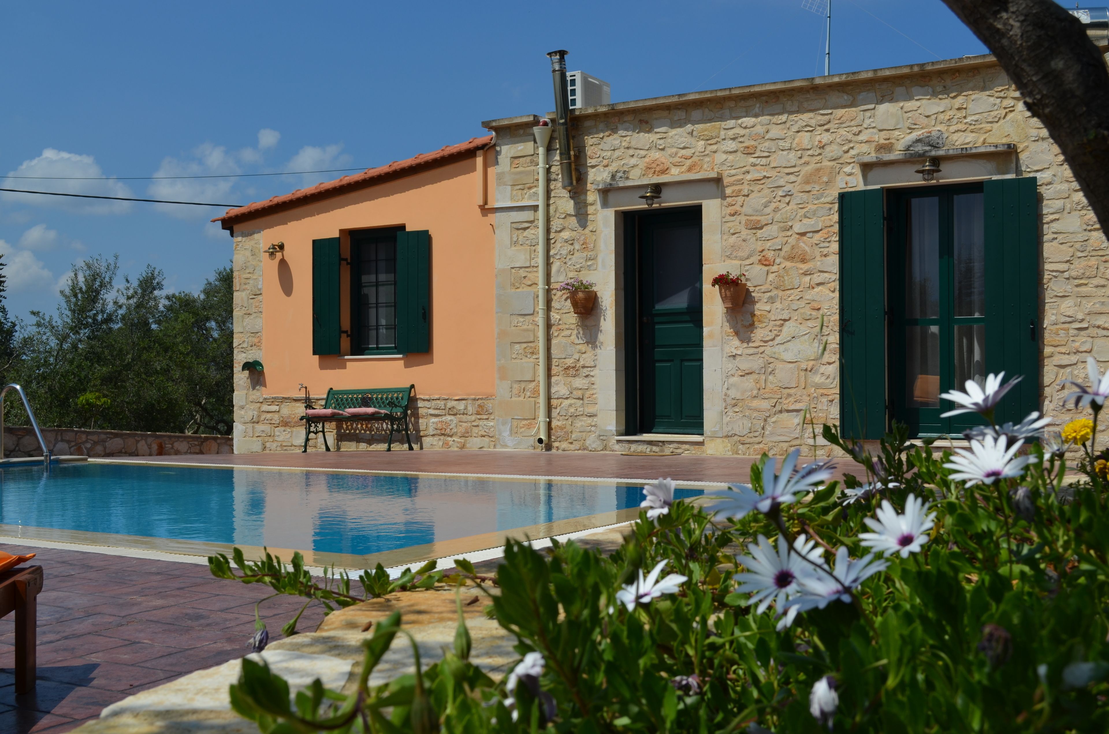 A stone building with a swimming pool, a bench, and a door with green shutters.