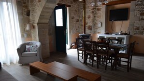 Una sala de estar acogedora con un banco de madera, una mesa de comedor con sillas, una pared de piedra, un televisor montado sobre una encimera de cocina y una puerta que da a otra habitación.