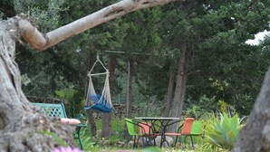 Una hamaca colgada entre árboles, una mesa con sillas y un muro de piedra en un jardín.