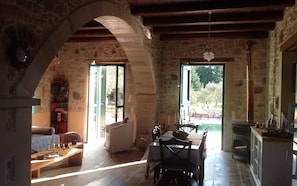 A rustic interior with stone walls, a dining area with a table and chairs, a sofa, and a fireplace.