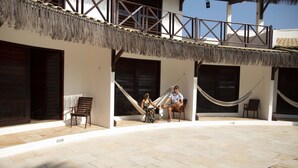 A covered outdoor area with a stone floor, two hammocks, and a wooden bench. - Pousada Porto Azul (Caucaia)