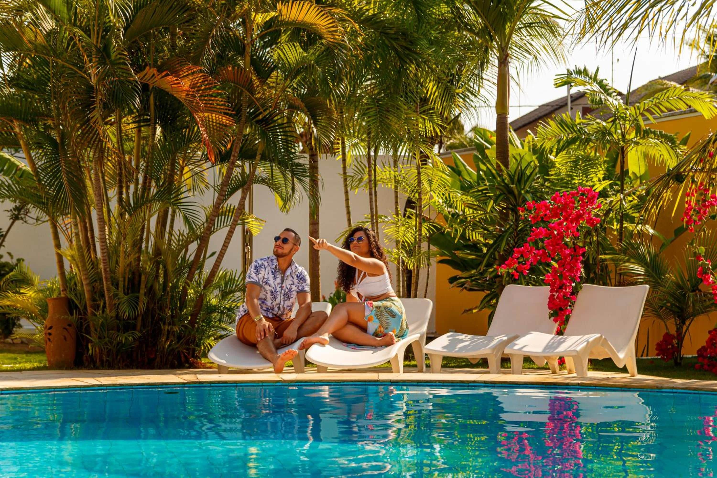 Zona de piscina con sillones de descanso, una piscina cristalina y vegetación tropical.