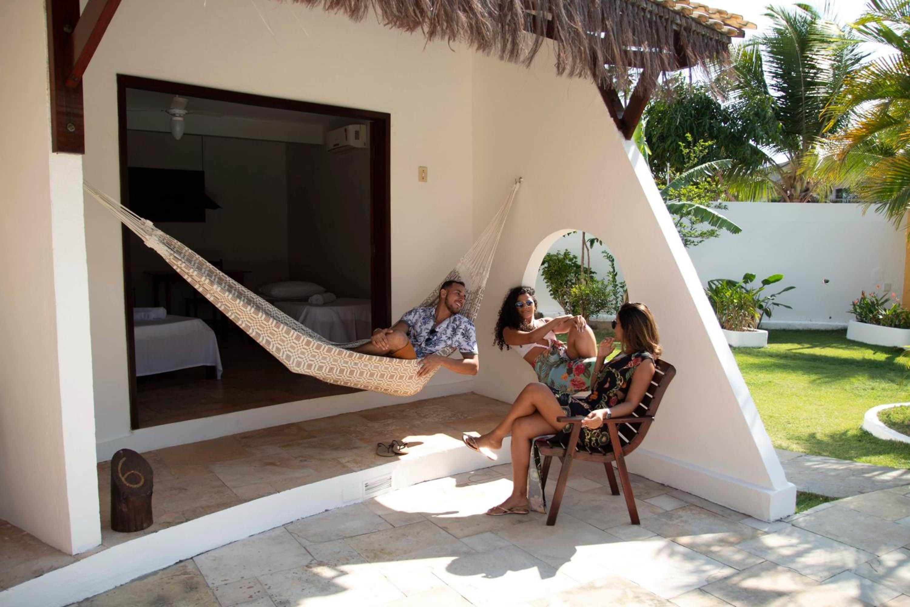 A hammock in a covered outdoor area with a bed and a chair.