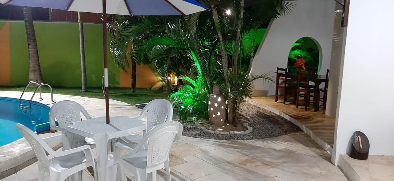 An outdoor pool area with a table and chairs, surrounded by palm trees and decorative lights.