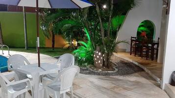 An outdoor pool area with a table and chairs, surrounded by palm trees and decorative lights.