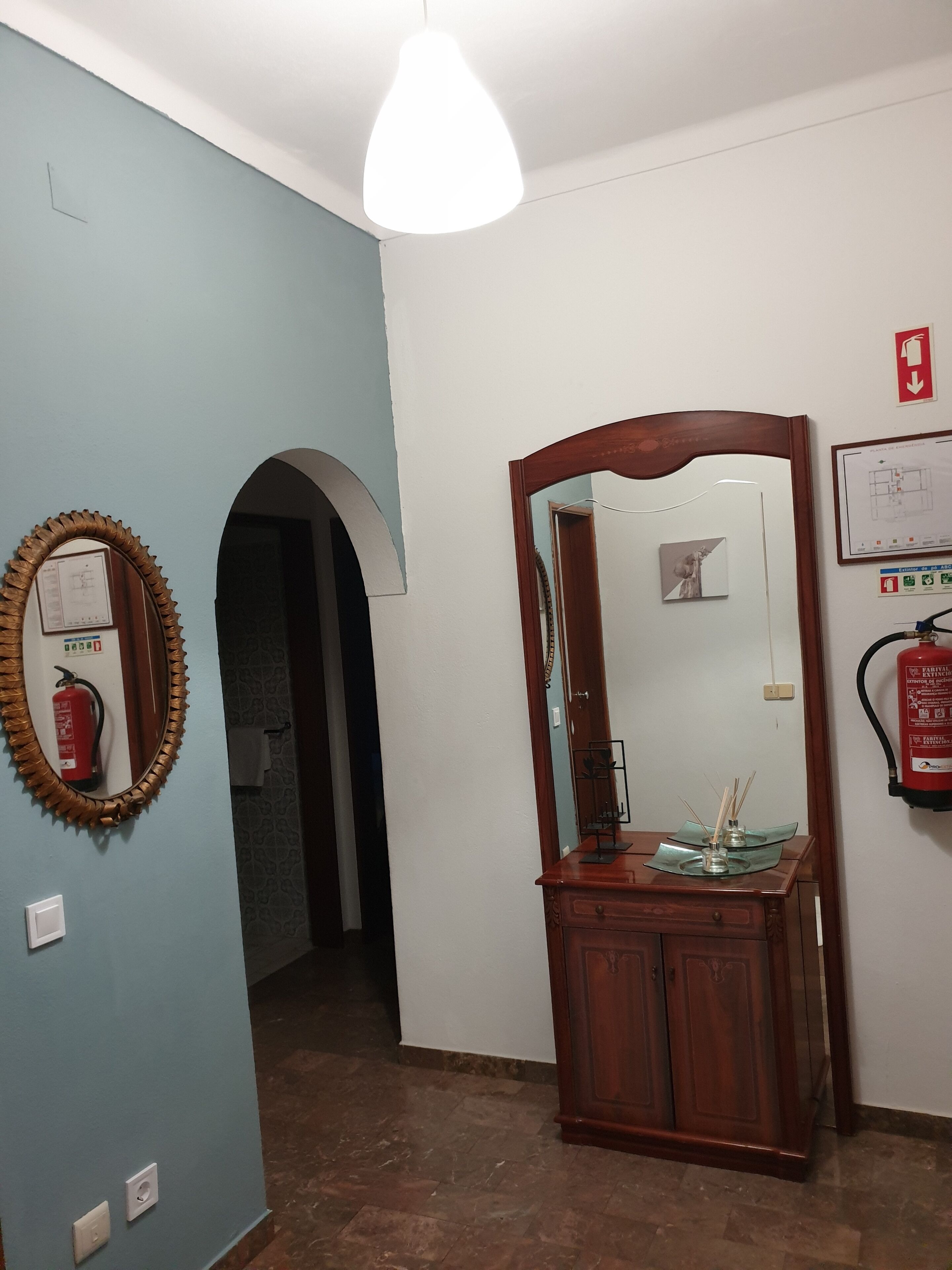 A hallway with a wooden cabinet, a mirror, and a fire extinguisher on the wall.