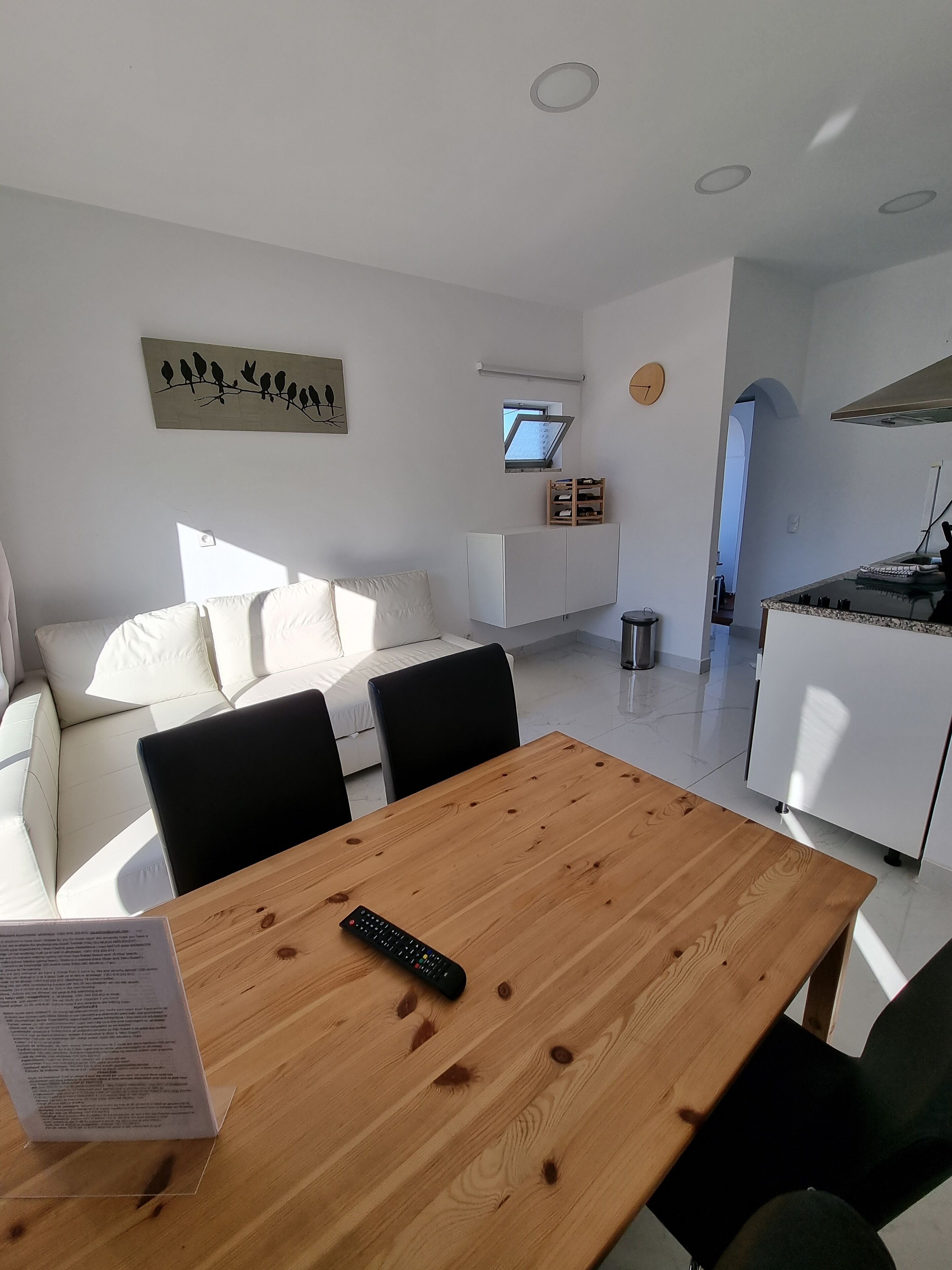 A modern living room with a wooden dining table, white sofa, and a painting of birds on the wall.