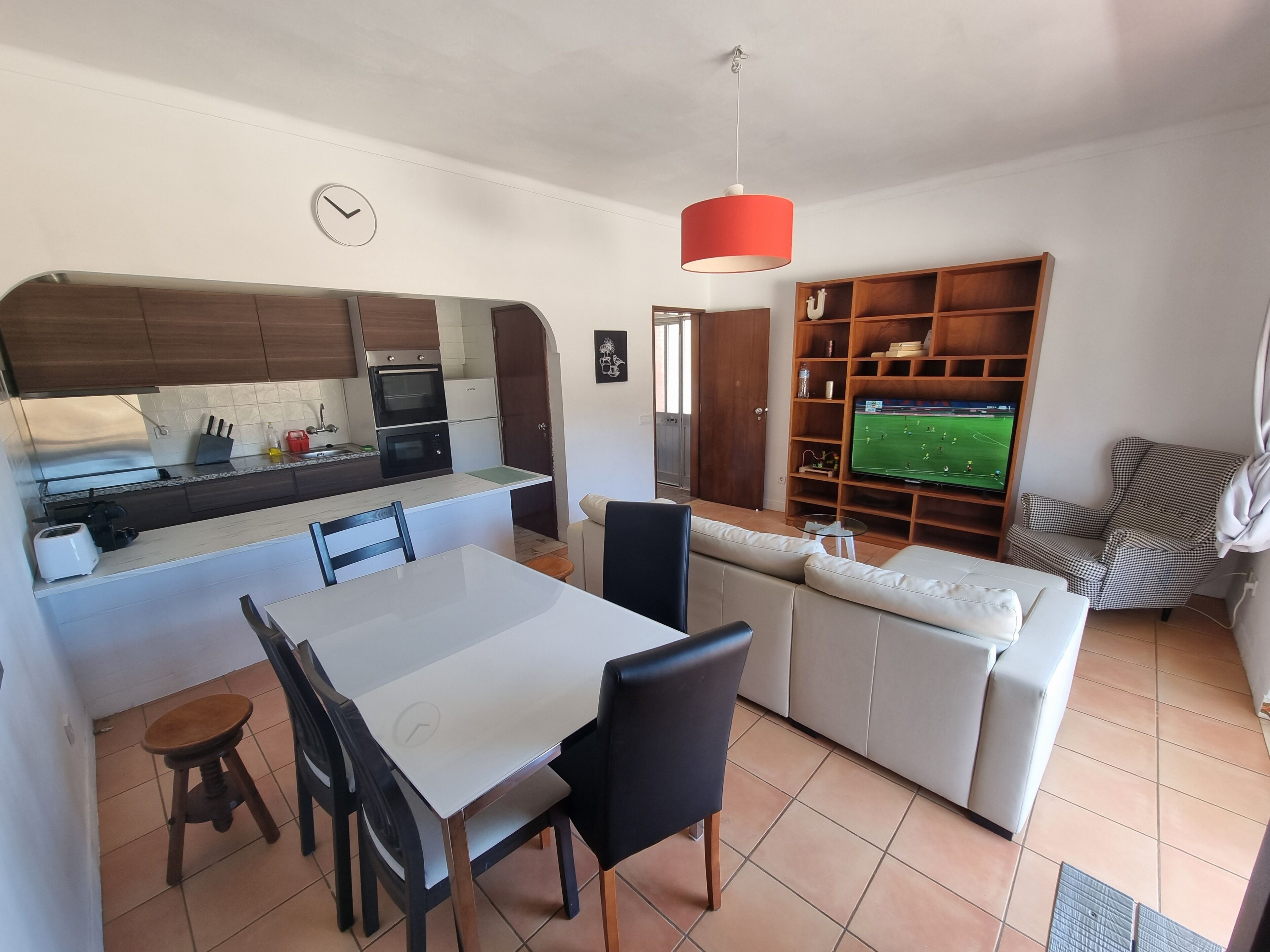A modern kitchen with a dining area, a sofa, and a TV in the living room.