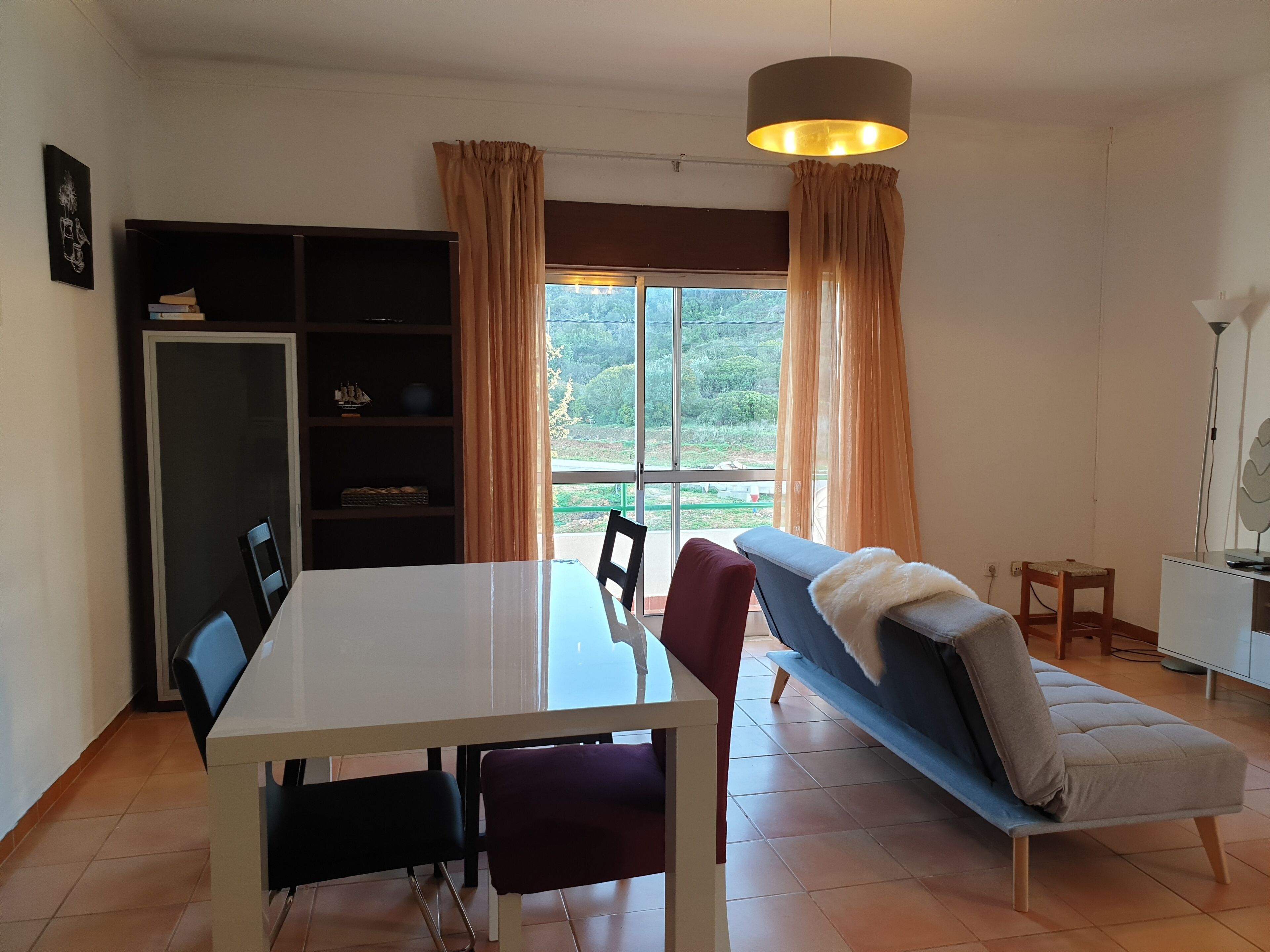 Un comedor con una mesa y sillas, un sofá, una estantería y vistas a zonas verdes al exterior.