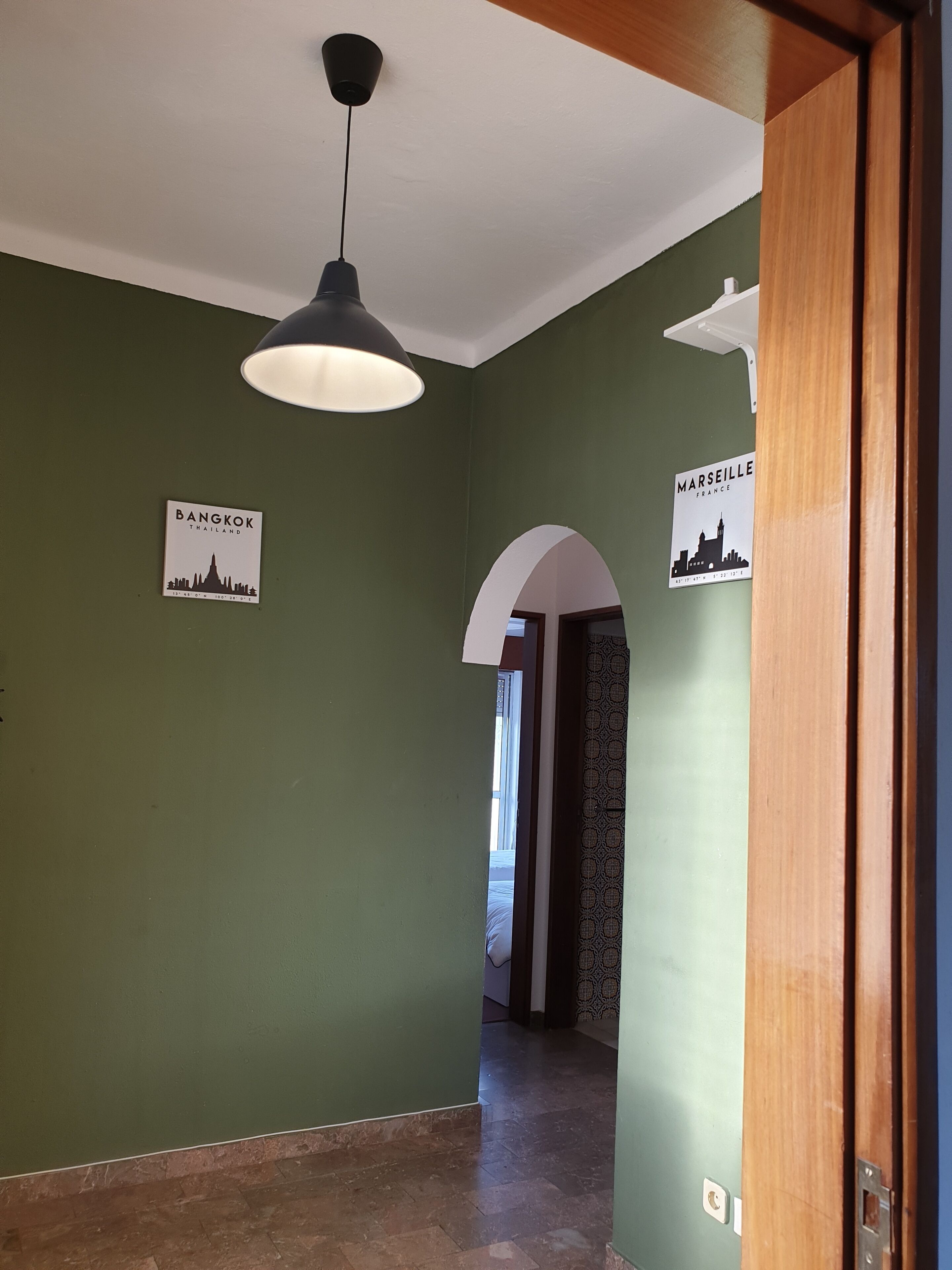 Een gang met groene wanden, een plafondlamp en twee borden die Bangkok en Marseille aangeven.
