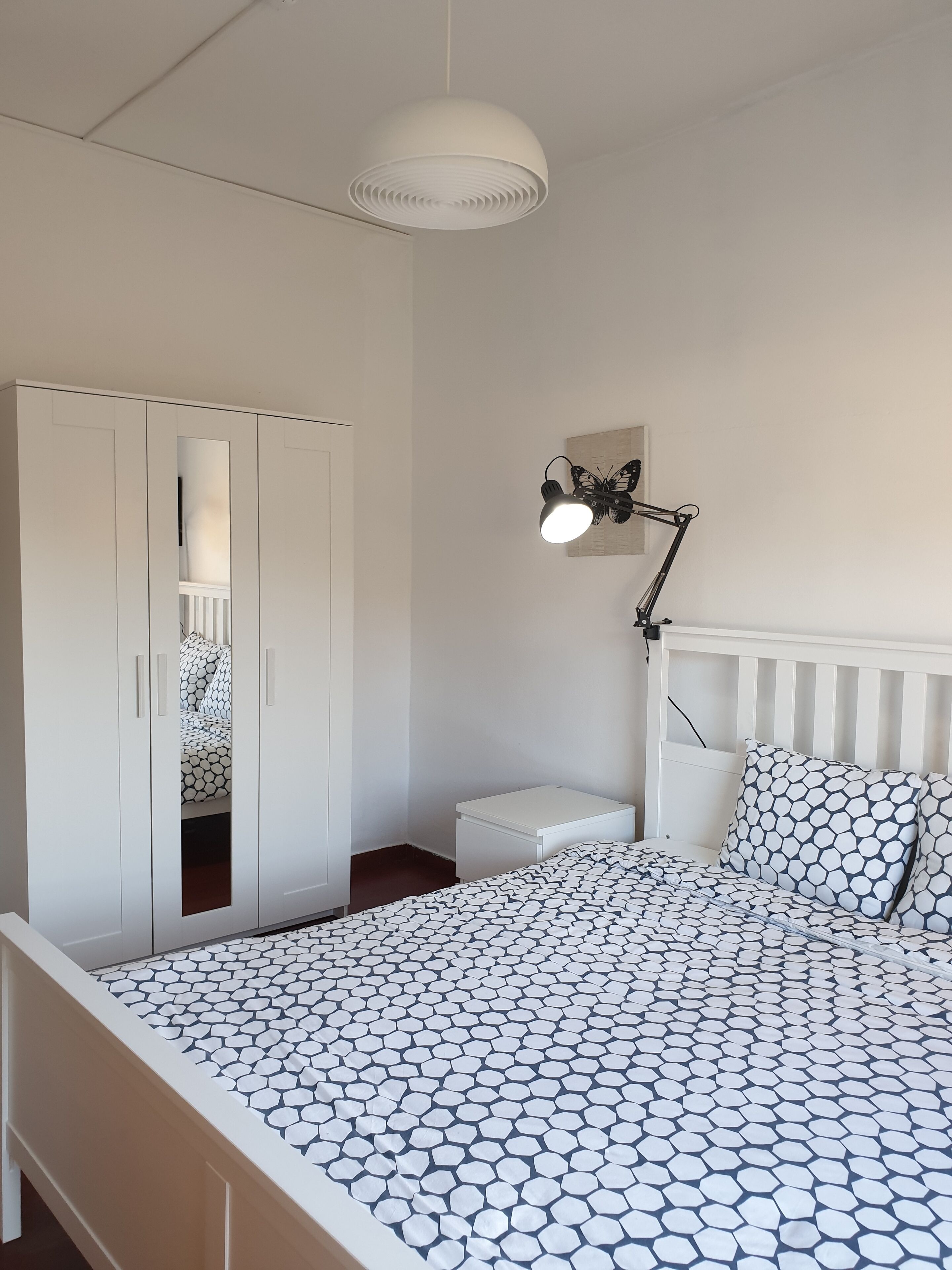 Une chambre à coucher comprenant un lit, une armoire, une table de chevet, une lampe et un luminaire au plafond.