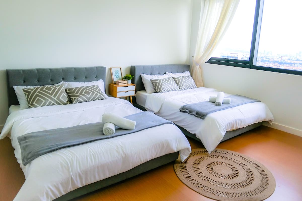 A hotel room with two beds, a small bedside table with a plant, and a view of the city through a window.