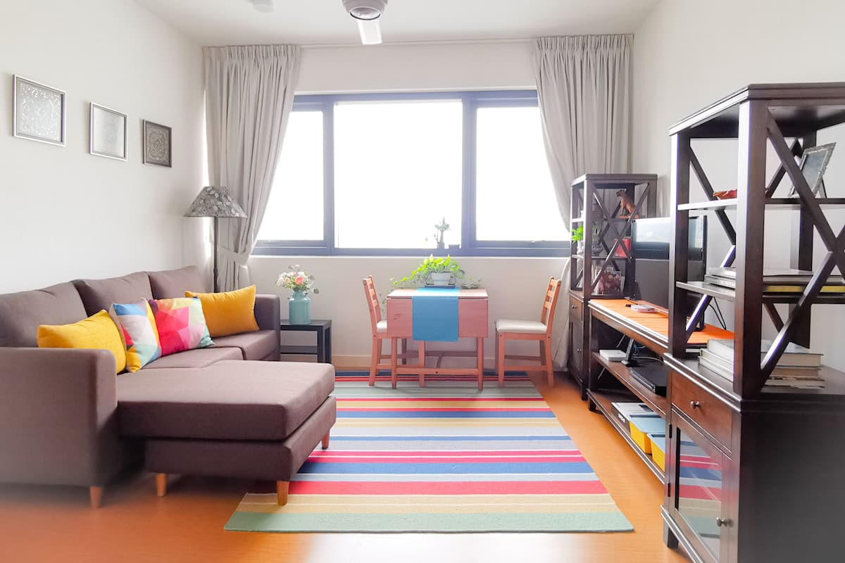 A living room with a sofa, a coffee table, a bookshelf, and a window with curtains.