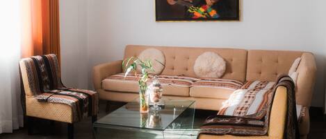 Una sala de estar con un sofá color beige, dos sillones, una mesa de centro de vidrio y un cuadro en la pared.