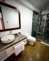 A modern bathroom with a round sink, a toilet, and a glass shower enclosure.