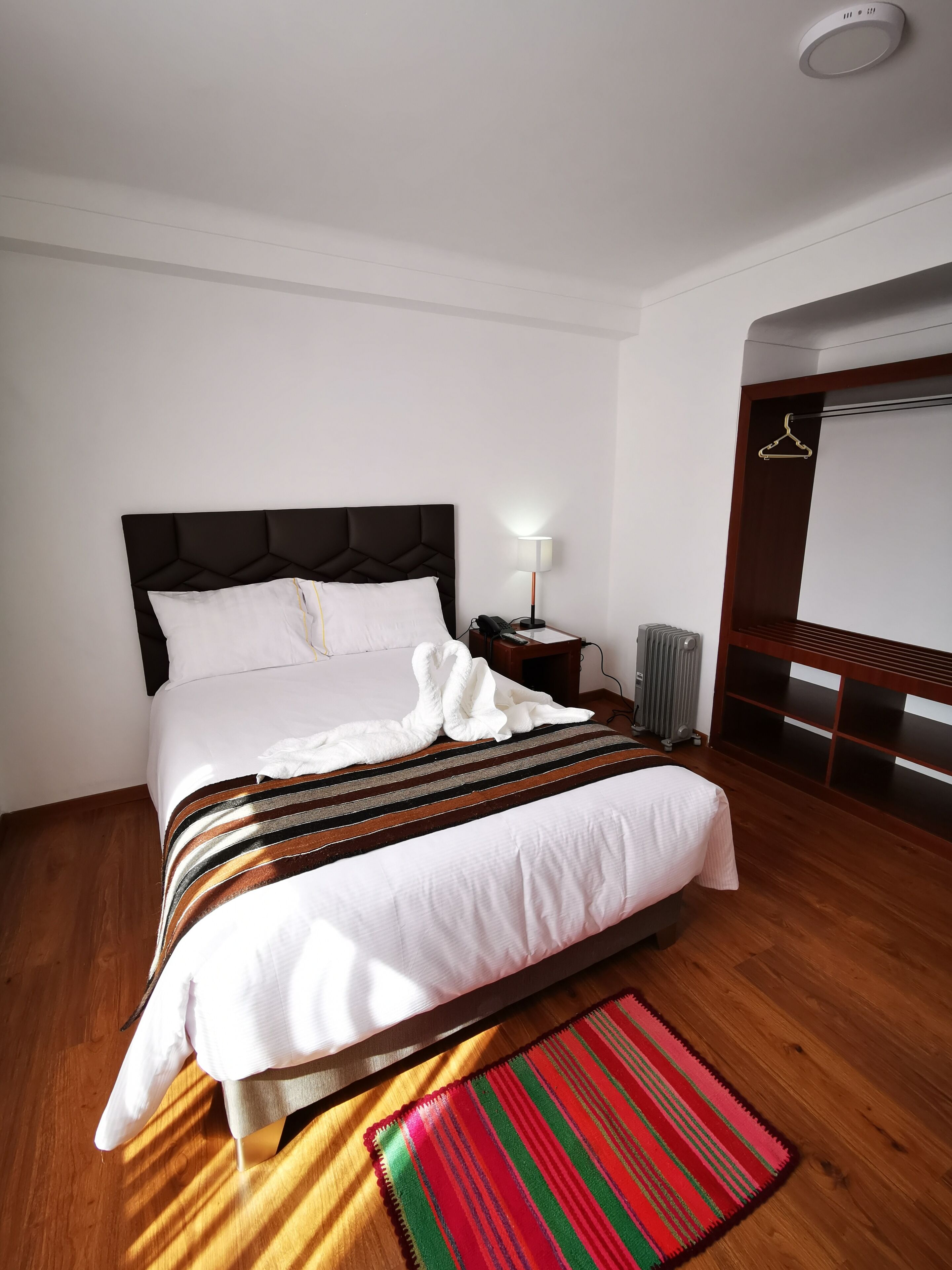 Een net opgemaakt bed met een gestreept dekbed, een bedlampje en een houten vloer.