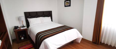 Una cama bien hecha con una colcha a rayas, una mesita de noche con una lámpara y un pequeño marco de fotos en la pared.