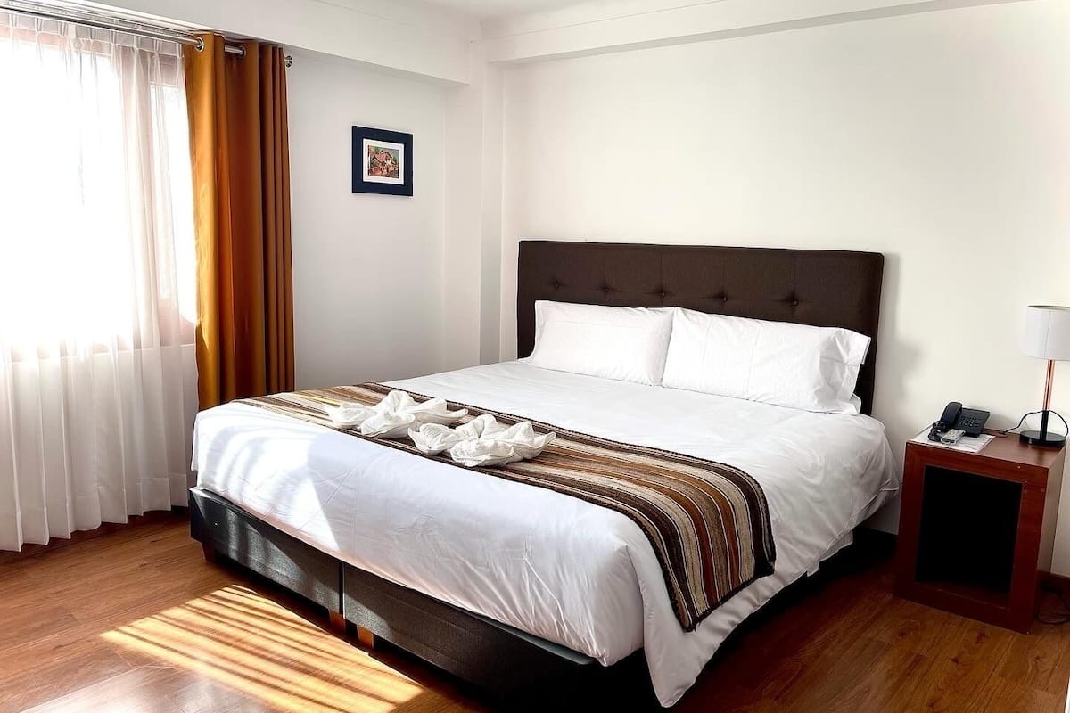 A hotel room with a large bed, a bedside table with a lamp, and a framed picture on the wall.