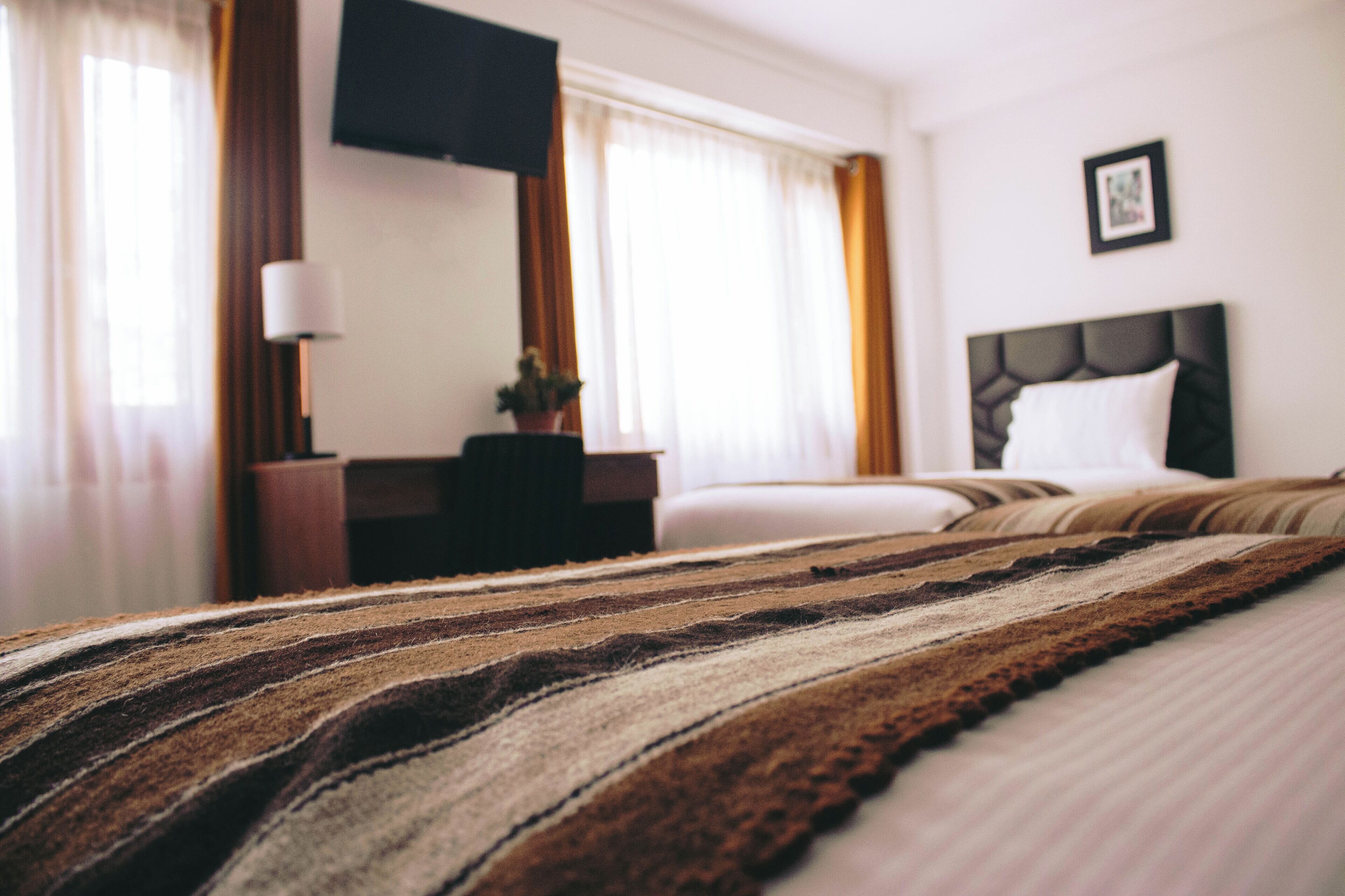 Habitación de hotel con cama, mesita de noche, lámpara, televisión y ventana con cortinas.
