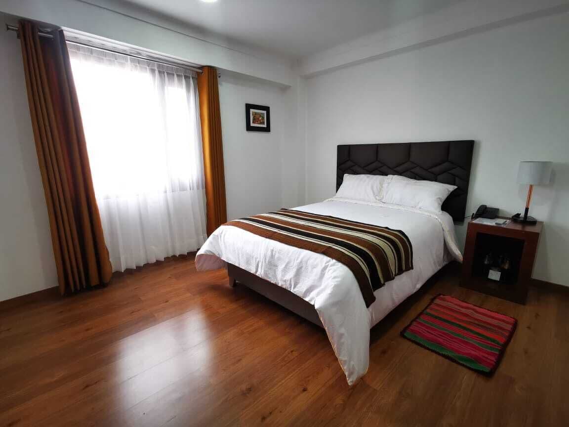 A bedroom with a bed, a nightstand, a lamp, a window with curtains, and a framed picture on the wall.