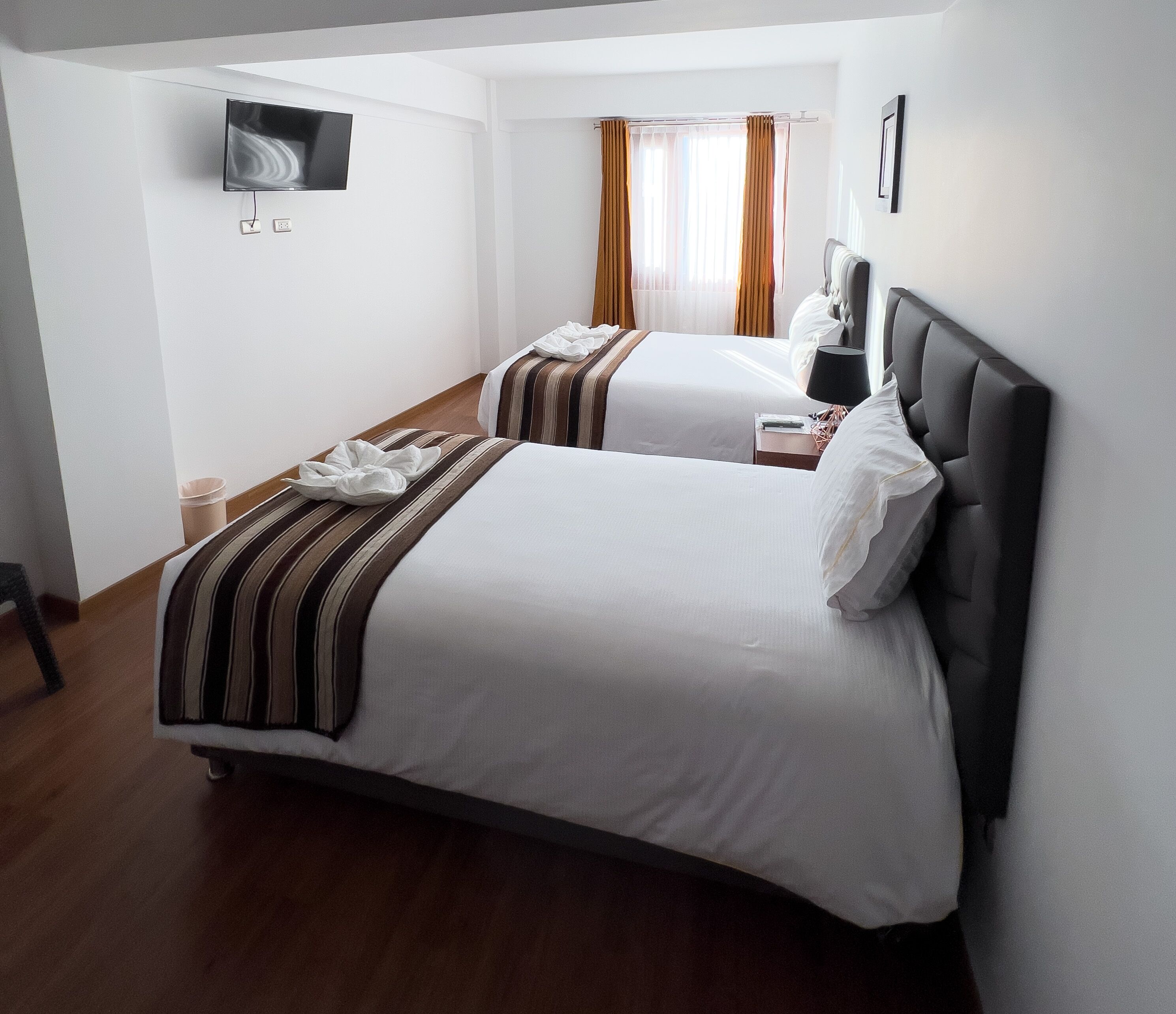 A hotel room with two beds, a flat-screen TV mounted on the wall, and a window with curtains.