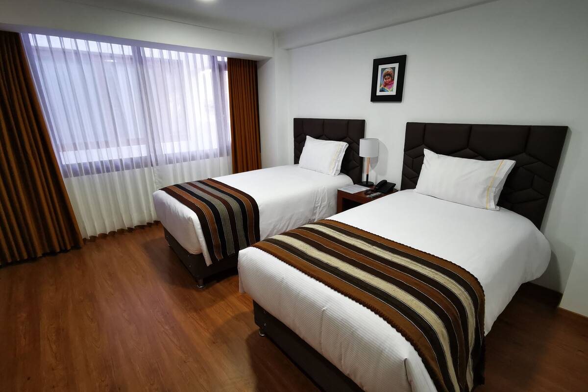 A hotel room with two beds, a nightstand, a lamp, and a framed picture on the wall.