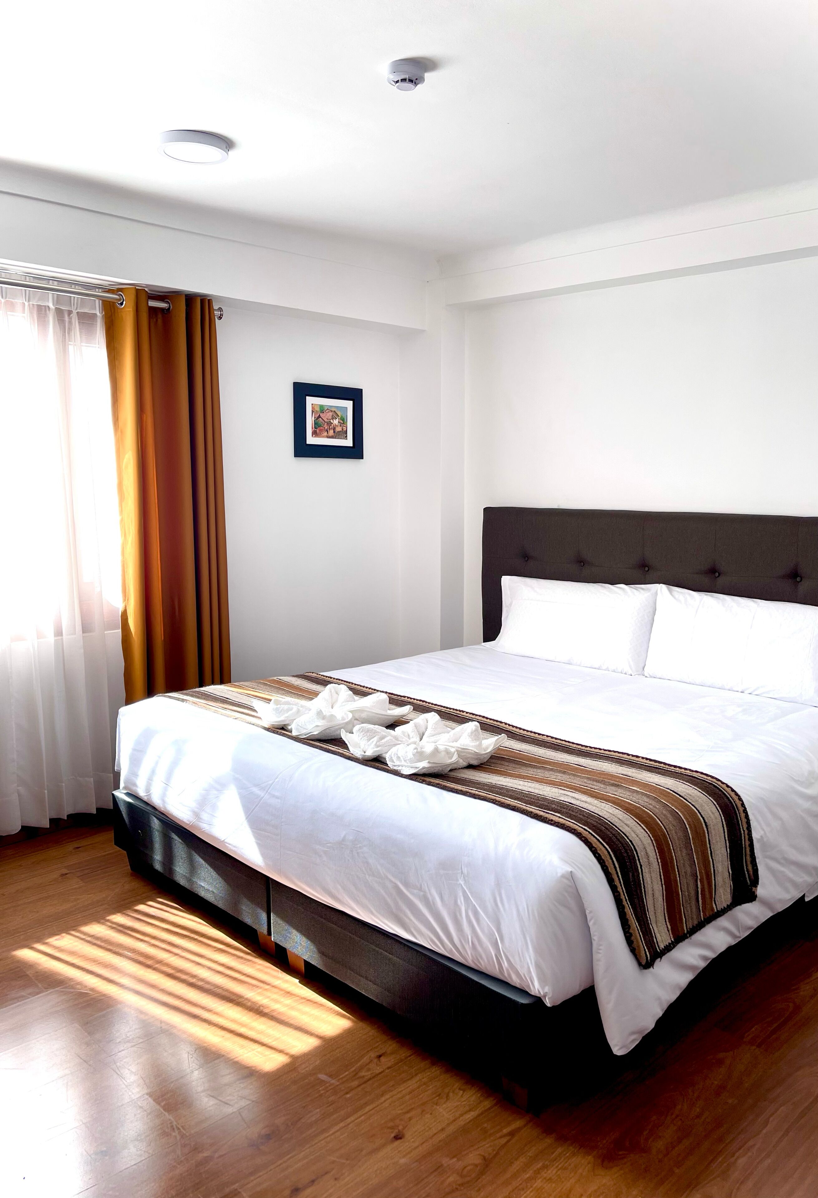 A neatly made bed with a striped blanket, a dark headboard, and a framed picture on the wall.