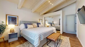 A bedroom with a large bed, bedside tables, a bench, a mirror, and a TV on the wall. - Pet-Friendly & Remodeled, Gas Grill, Near the New Rec Center, On-site Pool (Mammoth Lakes)