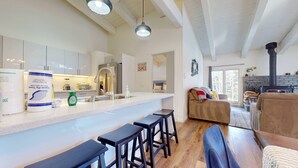 Une cuisine moderne dotée d’un îlot central, de tabourets de bar et d’un coin repas comprenant un canapé et une cheminée.
