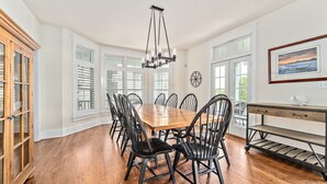 A dining room with a wooden table and chairs, a chandelier, and a view of the outdoors through large windows. - 5-bedroom vacation home just a short walk to Cape May Beach (Cape May)