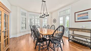 Une salle à manger avec une table et des chaises en bois, un lustre et une vue sur l’extérieur grâce à de grandes fenêtres.