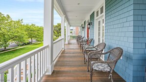 A covered porch with wicker furniture and a view of a green lawn and buildings in the distance.