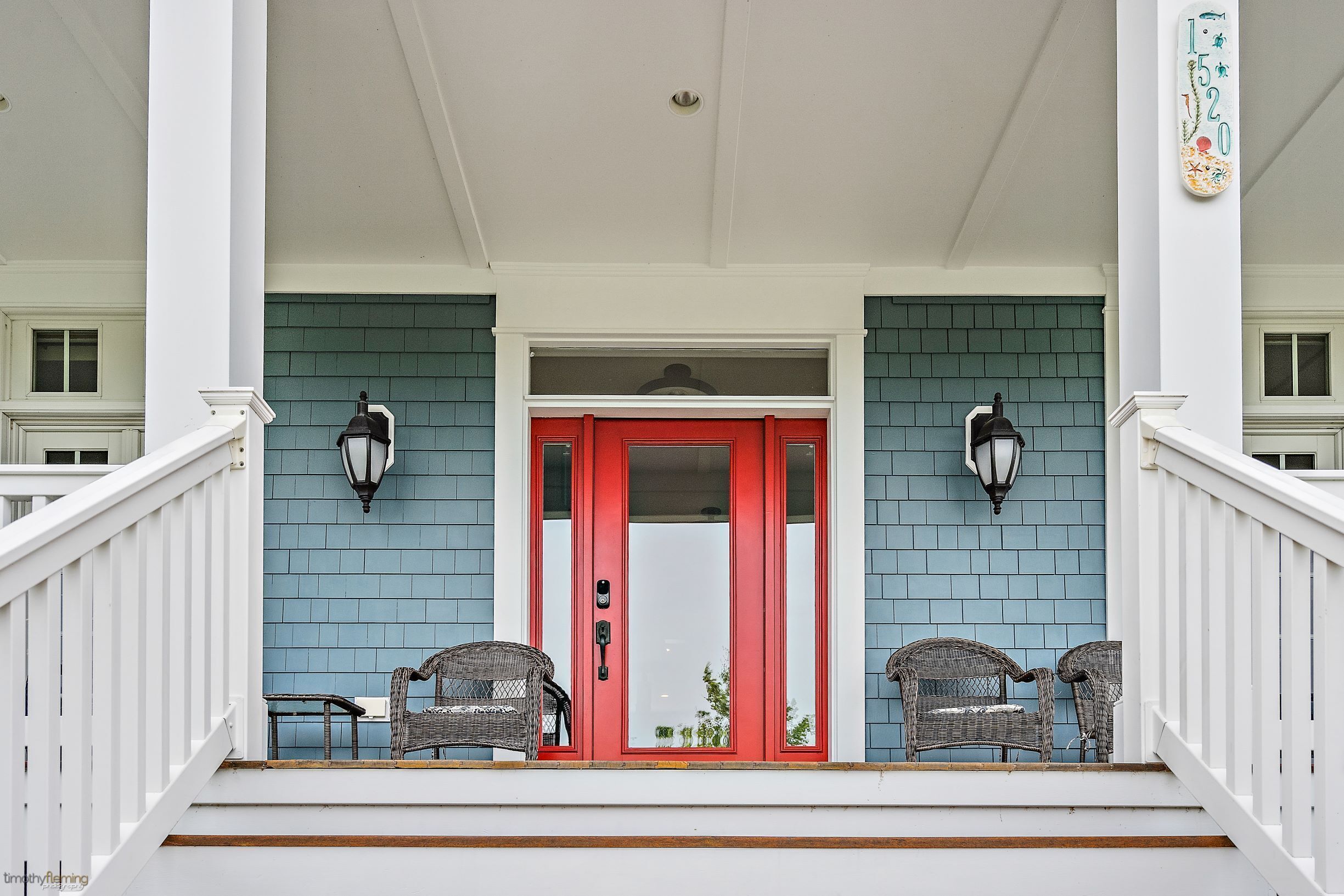 A porch with a red door, two wicker chairs, and a blue brick wall.
