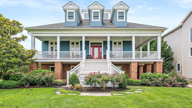 A two-story house with a front porch, brick foundation, and a red door.