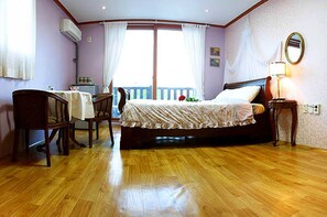 A bedroom with a wooden floor, a bed with a floral bedspread, a desk with a chair, and a window with curtains.