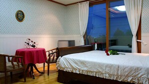 Un dormitorio con una cama, una mesa con mantel rojo, una silla y una ventana con cortinas.