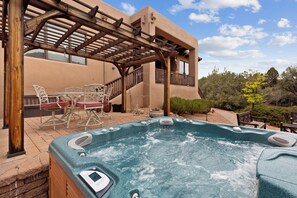 Ein Whirlpool mit Bedienfeld, eine Holzpergola, Gartenmöbel und ein Gebäude mit Balkon.