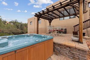 Ein Whirlpool unter einer Holzpergola, eine Steinmauer und Terrassenmöbel.