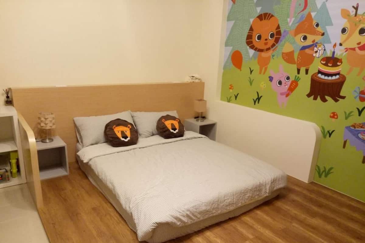 A bedroom with a bed, two pillows with animal faces, a nightstand, a wall mural, and a wooden floor.
