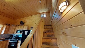 Een houten chalet van binnen met een keukenhoek, houten trap en een klein raam.