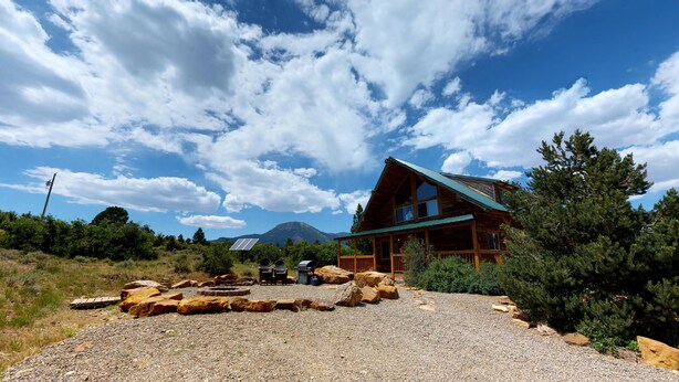 A cabin with a sloped roof, surrounded by a gravel area with large rocks and a solar panel. - Canyon View Family Lodge (Monticello)