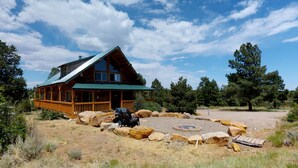 A log cabin with a green roof, surrounded by a gravel area with large rocks and a fire pit. - Canyon View Family Lodge (Monticello)
