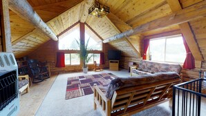 A cozy log cabin interior with a wooden ceiling, a sofa, a television, and a fireplace. - Canyon View Family Lodge (Monticello)