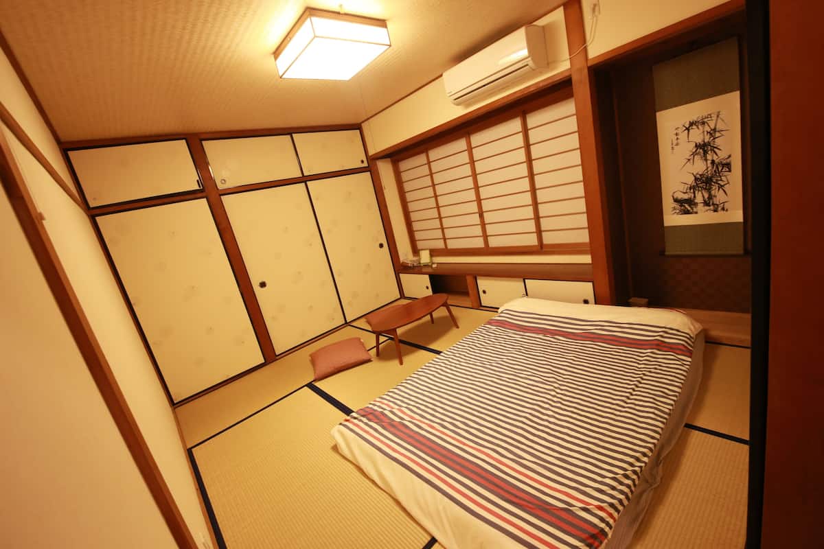 Een traditionele Japanse kamer met tatami vloerbedekking, een bed met gestreept beddengoed, een houten bureau en een shoji scherm.